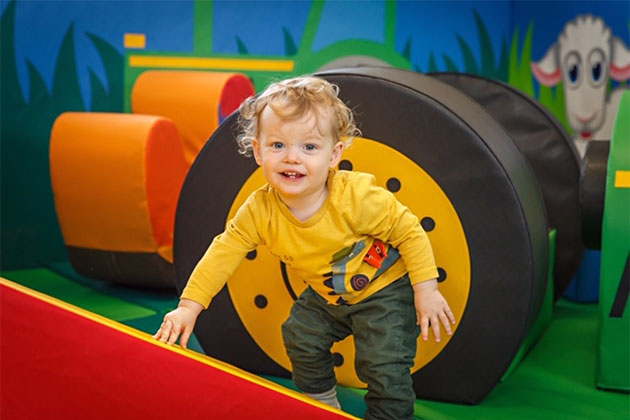 Slide in the soft play area, with small child looking happy to try and climb up it