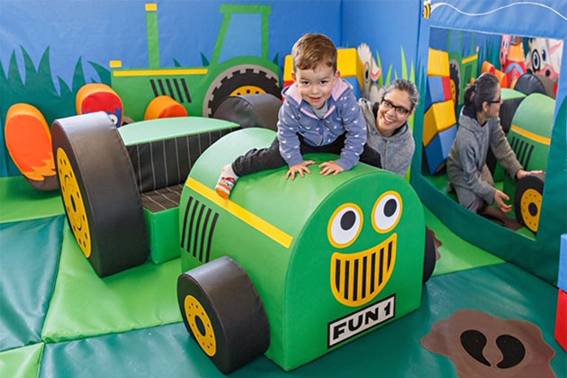 Child astride the simplified front of a tractor, with attentive smiling mum